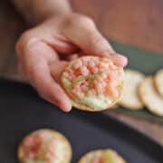 Hand holding cracker with almond cheese and dollop of vegan caviar.