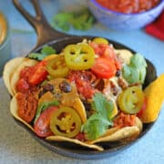 Nachos with vegan queso, salsa, black beans, and jalapeno pepper slices in cast iron skillet.
