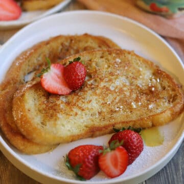Eggless French toast on plate with maple syrup and strawberries.