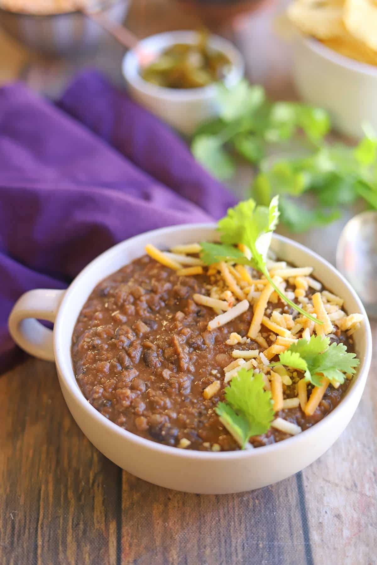 Lentil chili topped with vegan cheese shreds and cilantro on table.