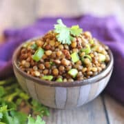Marinated lentils with green onions and sun-dried tomatoes in striped bowl, garnished with cilantro.