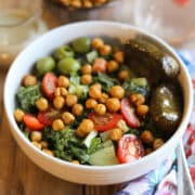 Massaged kale salad with roasted chickpeas, cherry tomatoes, Castelvetrano olives, and dolmas in a bowl.
