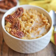 Pumpkin oatmeal in bowl with candied pecans, cinnamon, and a drizzle of non-dairy milk.
