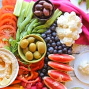 Tomatoes, sugar snap peas, olives, hummus, bell peppers, and blueberries on rainbow fruit and veggie tray.