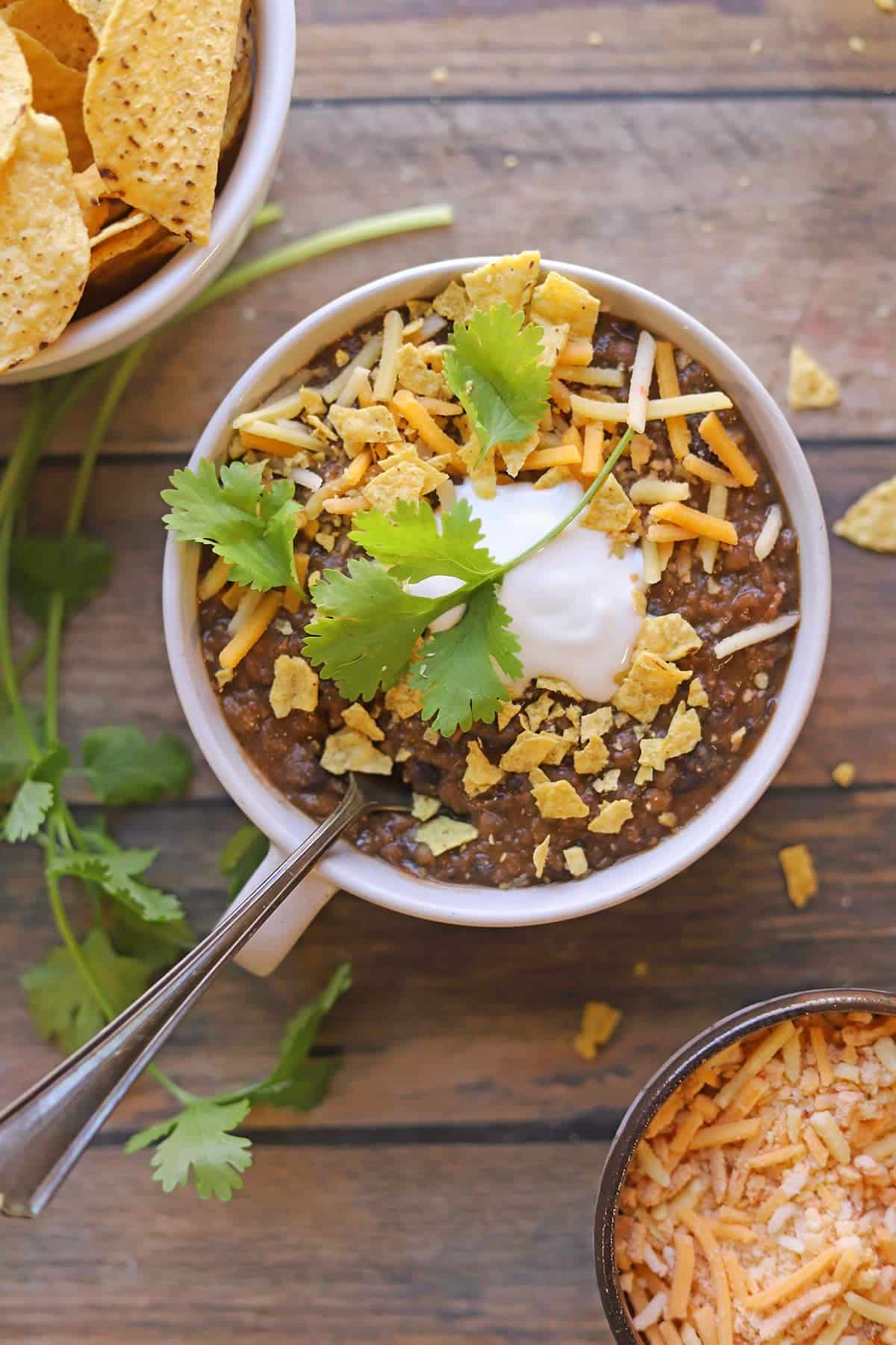 Vegan lentil chili with non-dairy sour cream, tortilla chips, shredded cheese, and cilantro.