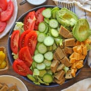 Rows of tomatoes, cucumbers, seitan, cucumber, and non-dairy cheese on vegan chef salad.