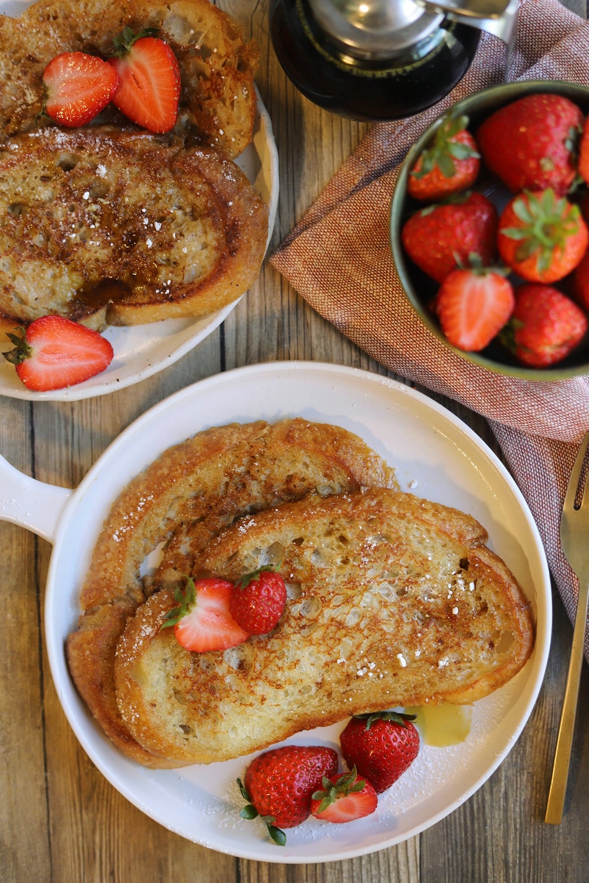 Vegan French toast on plates and topped with strawberries and powdered sugar.