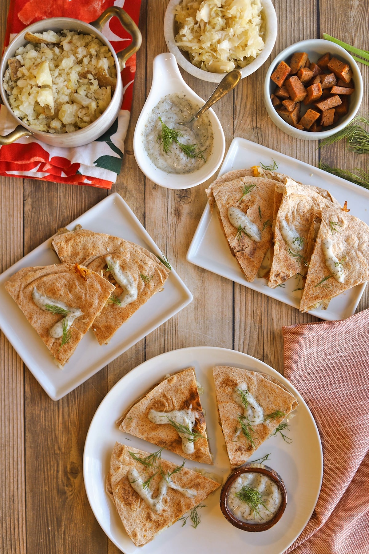 Mashed potatoes, sauerkraut, non-dairy yogurt ranch, vegan ham, and pierogi quesadillas on plates with fresh dill.