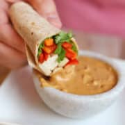 Spring roll tofu wrap being dipped into peanut sauce.