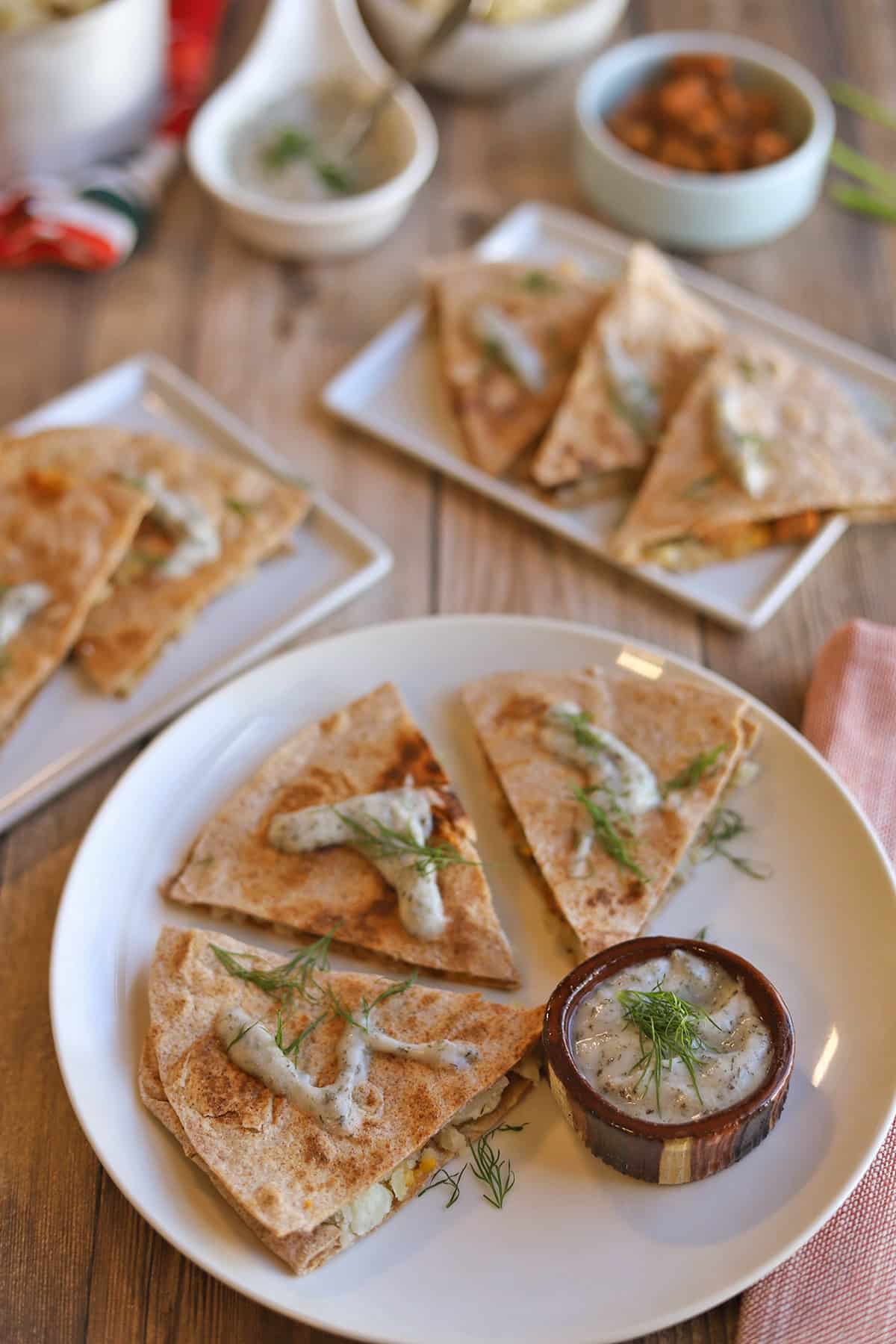 Several wedges of vegan pierogi quesadilla on table with toppings.