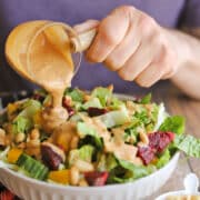 Tangy peanut salad dressing being poured onto colorful leafy green salad.