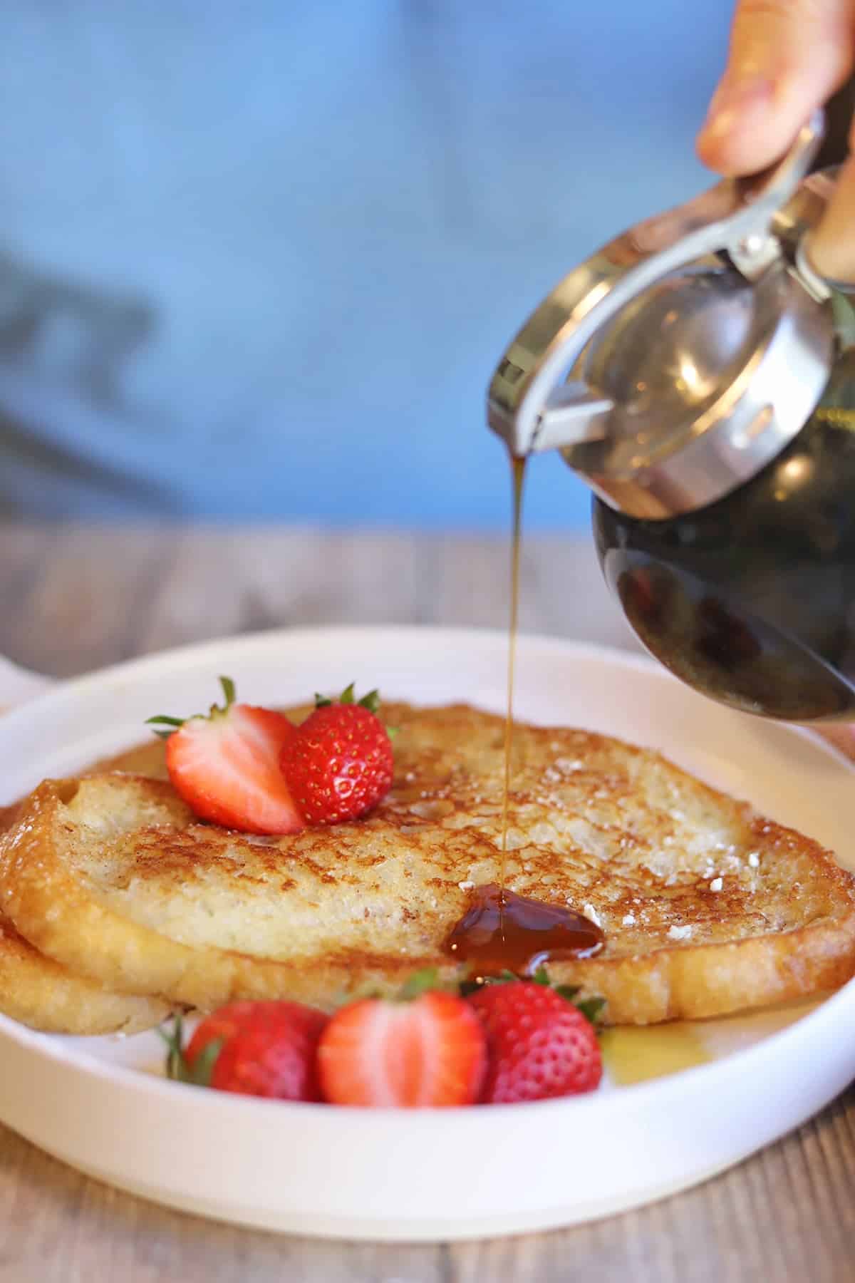 Maple syrup being poured over slices of vegan French toast with strawberries.