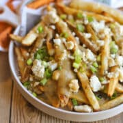 Baked fries on platter covered with vegan turkey gravy, almond feta, and green onions.