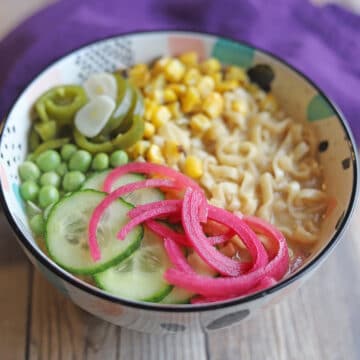 Vegan ramen with tahini broth topped with peas, corn, cucumbers, pickled jalapenos, and pickled red onions.