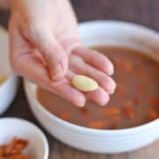 Hand holding skinned almond over bowl of almonds soaking in water.