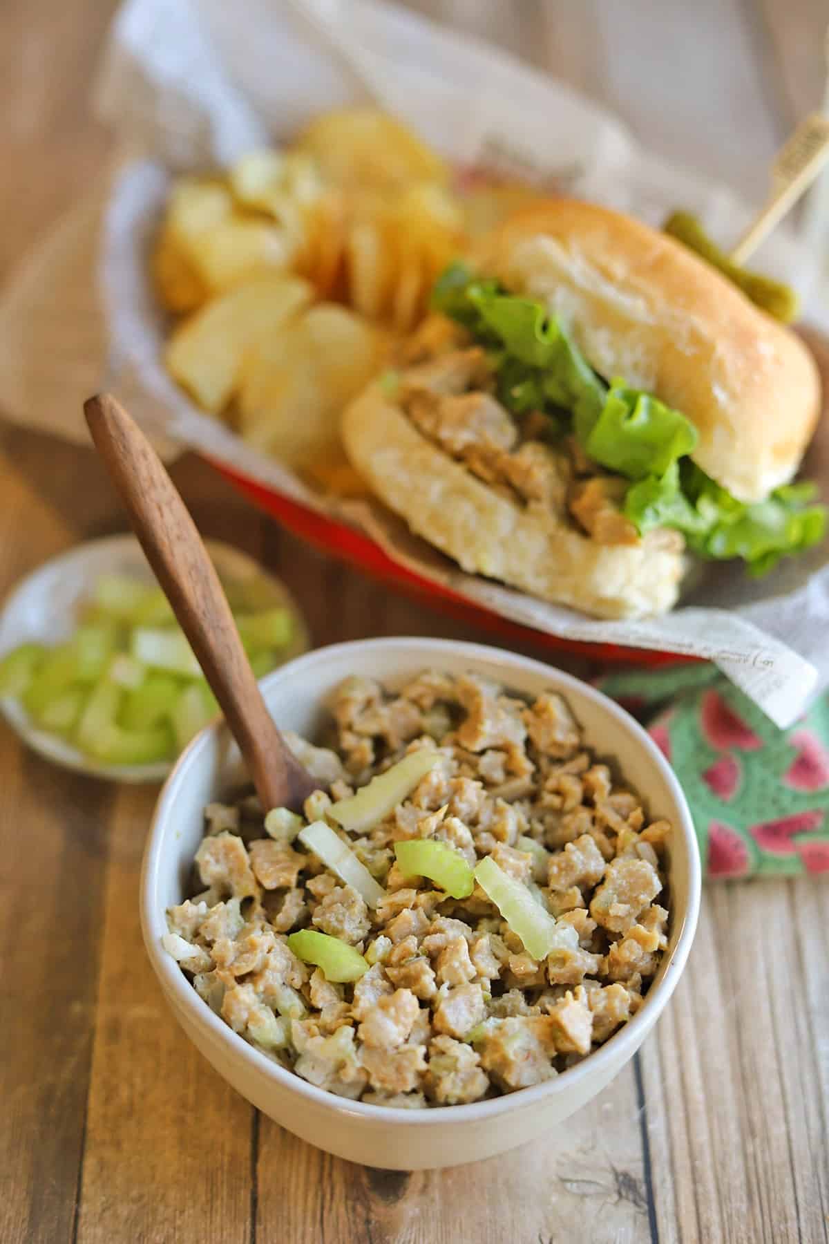 Seitan chicken salad in bowl with celery in front of seitan sandwich.