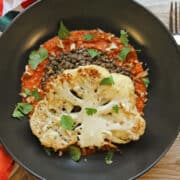 Roasted cauliflower in black bowl with romesco sauce and lentils.