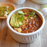 Meatless chili topped with avocado, tortilla chips, and vegan cheese in bowl.