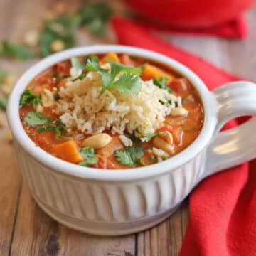 Sweet potato peanut stew in bowl, garnished with brown rice and cilantro.