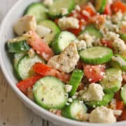 Tomato cucumber salad with vegan feta in white bowl.