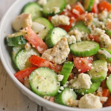 Tomato cucumber salad with vegan feta in white bowl.