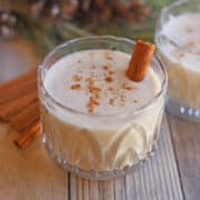 Vegan eggnog in glass with dash of cinnamon & cinnamon stick.