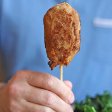 Hand holding vegan fried chicken leg on skewer.