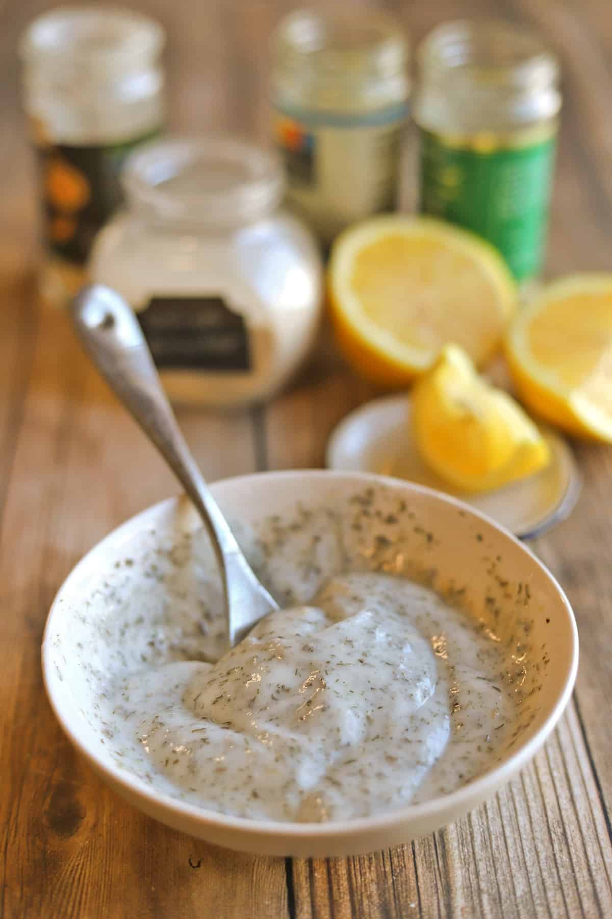 Yogurt ranch sauce being mixed in bowl by seasonings and lemon.