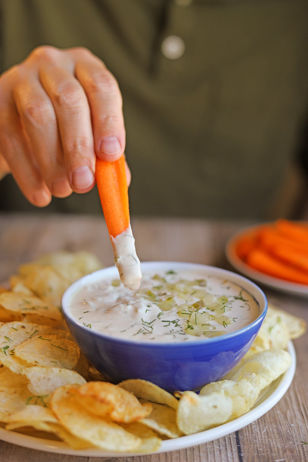 Carrot stick being dunked into dairy-free dill pickle dip.
