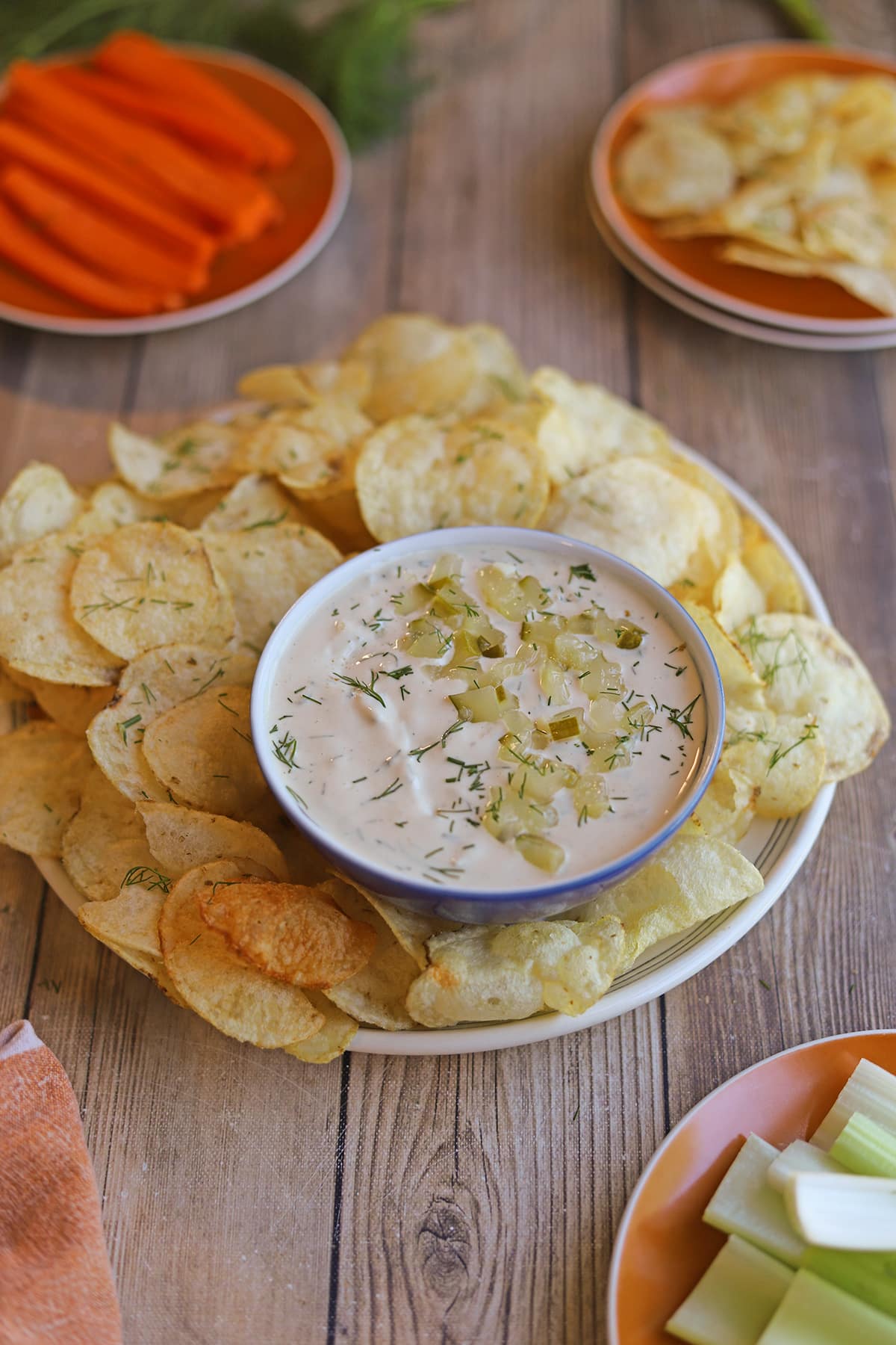 Platter of potato chips with vegan dill pickle dip, carrots, and celery.