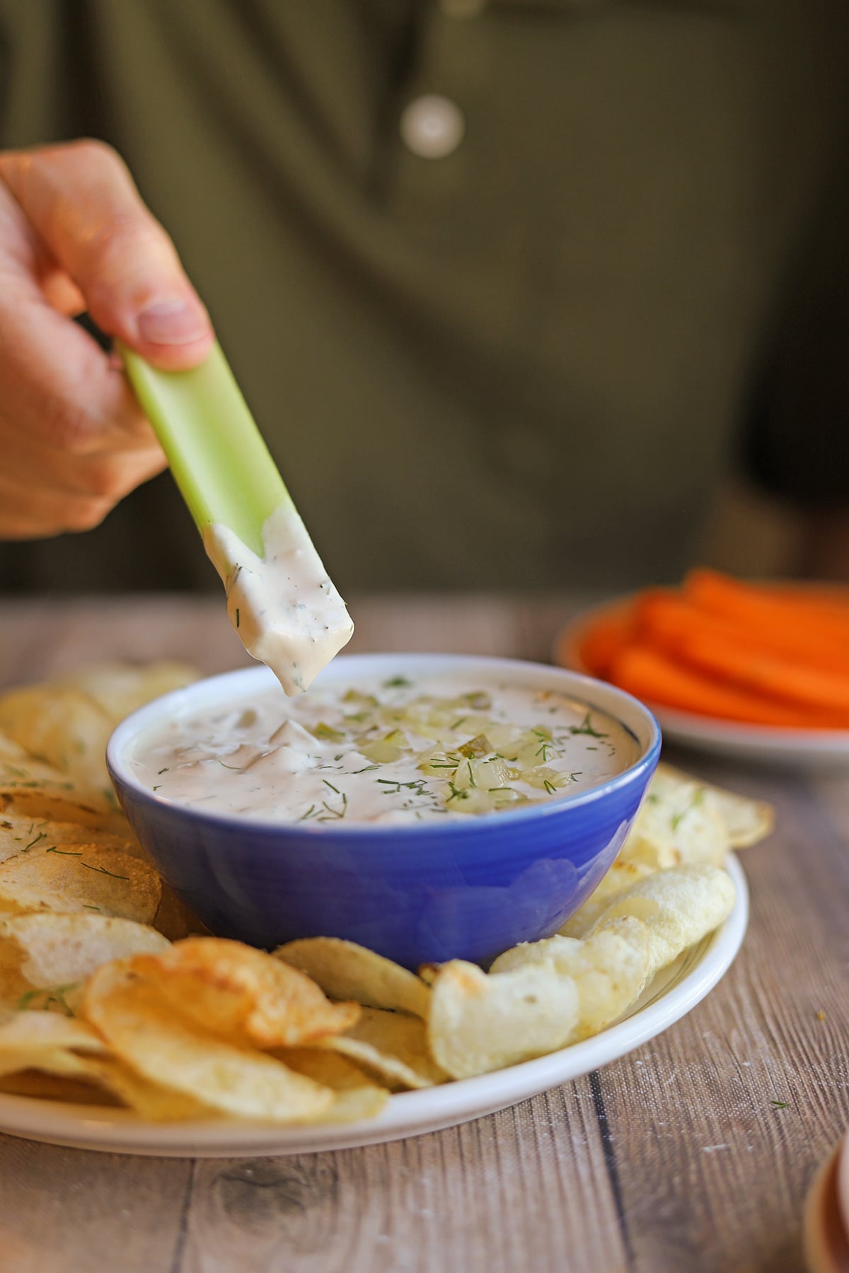 Celery dunked in creamy dill pickle dip with pickle and fresh dill garnish.