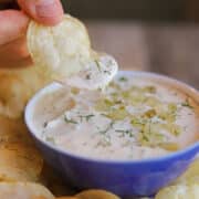 Potato chip dunked into creamy dill pickle dip with flecks of fresh dill and diced dill pickle.