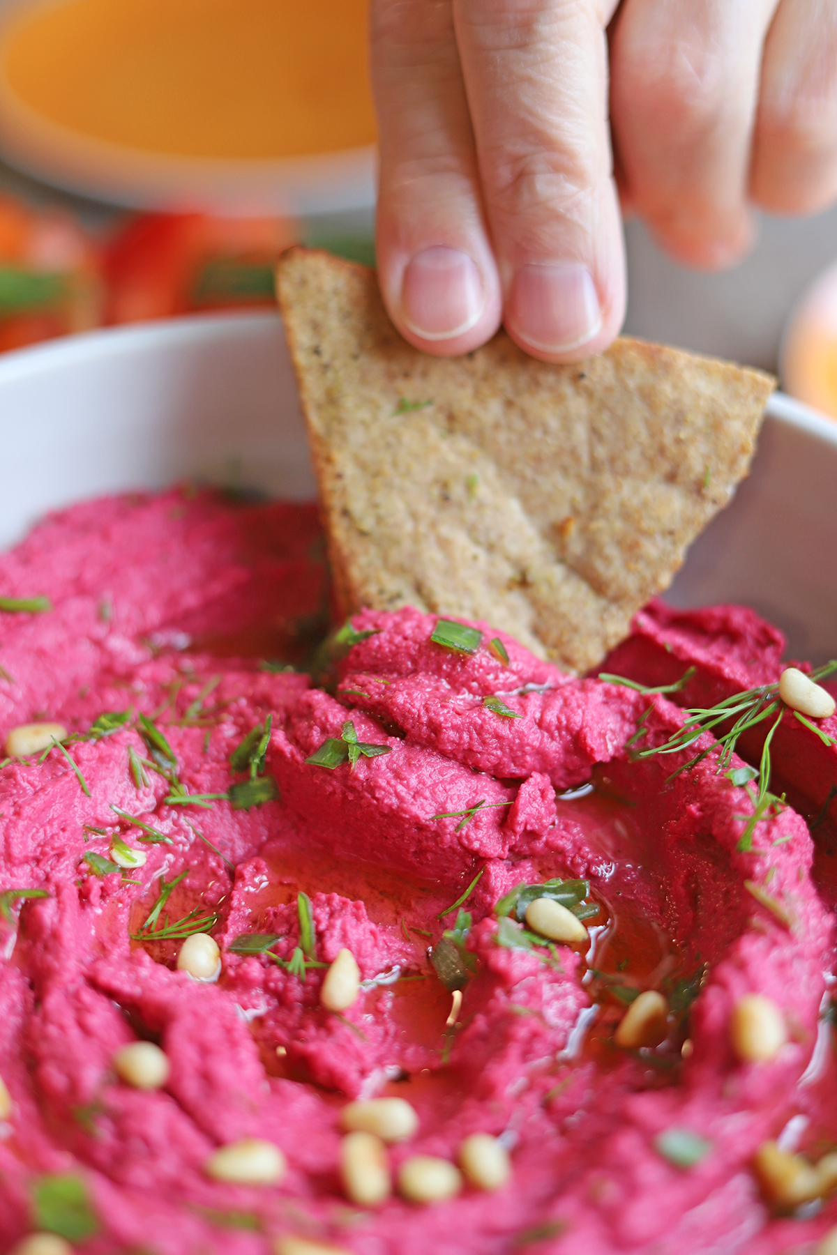 Air fryer pita chip being dunked into roasted beet hummus.