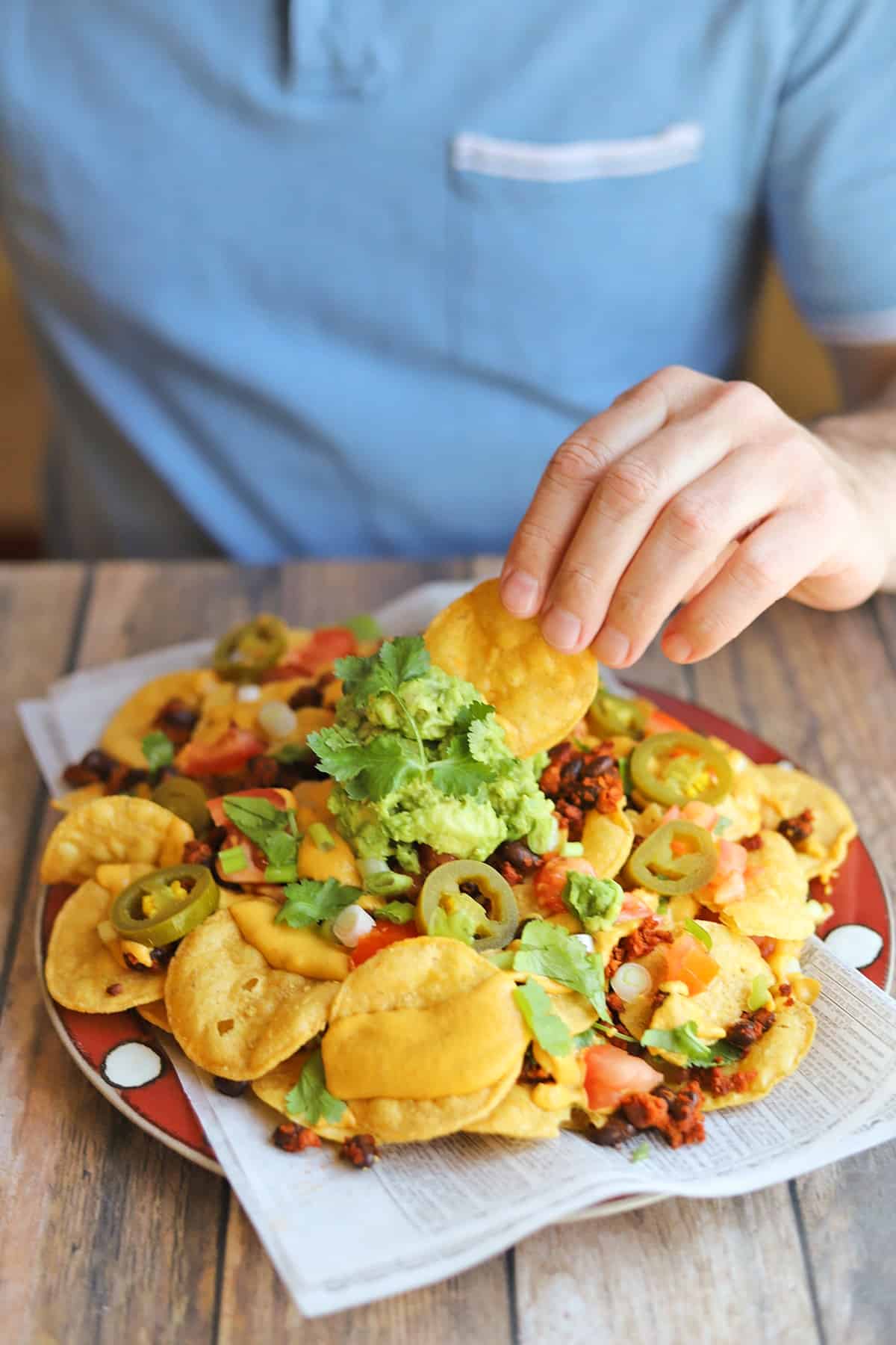 Hand dunking tortilla chip into guacamole on top of loaded vegan nachos.