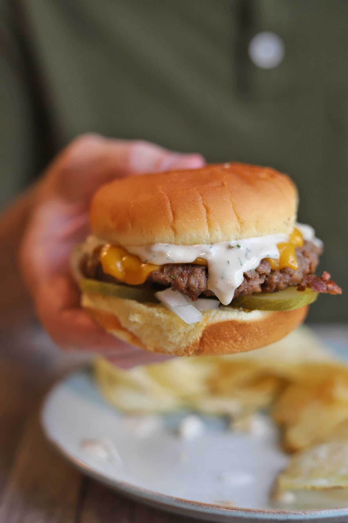 Pickle dip dripping down Impossible burger with non-dairy cheese, pickles, and onion on a potato bun.