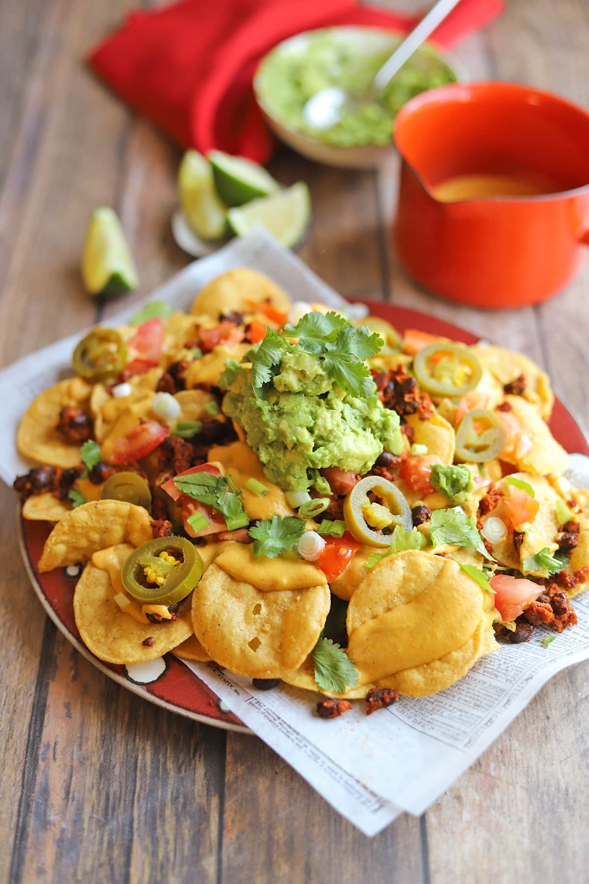 Platter of vegan nachos with vegan cheese sauce, guacamole, cilantro, and jalapeno peppers.