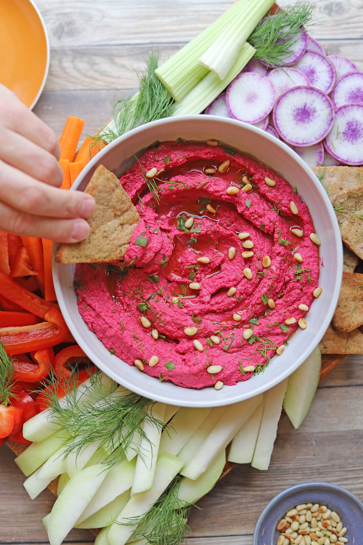 Hand dunking crunchy pita chip into bowl of air fryer roasted beet hummus on veggie board.