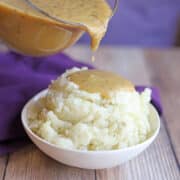 Vegan turkey gravy being poured onto bowl of creamy mashed potatoes.
