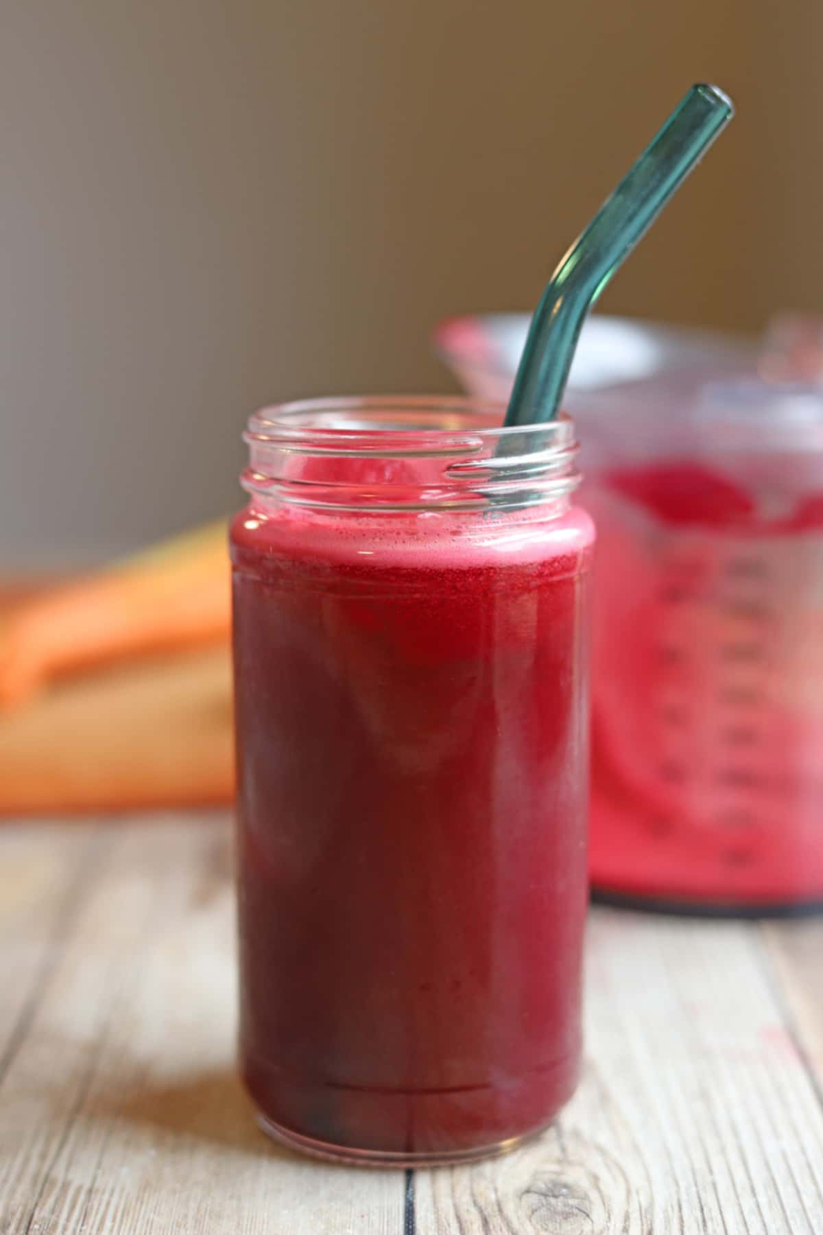Bright red glass of beet, carrot, apple juice on table with aqua straw.