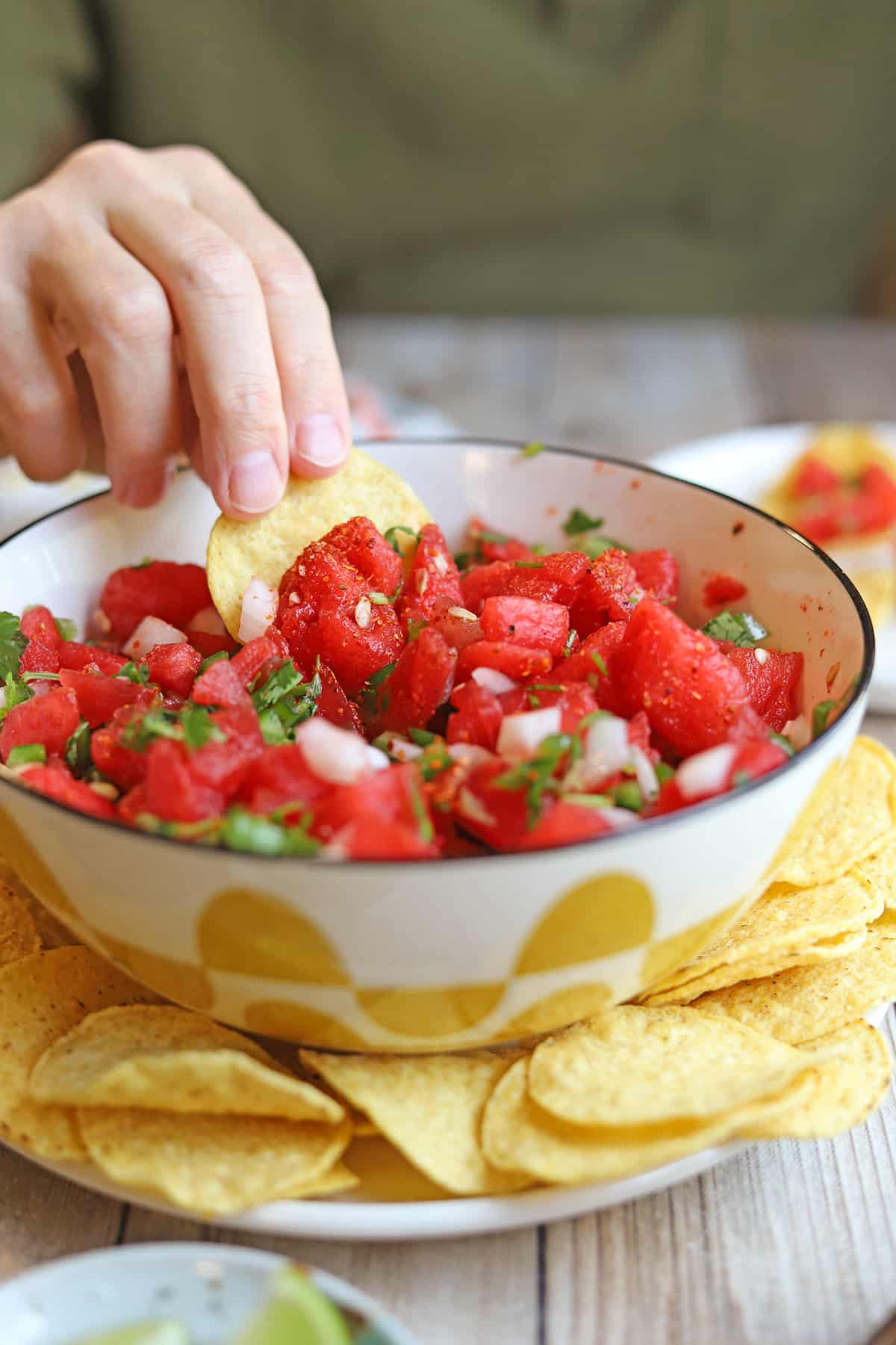 Tortilla chip being dunked into bowl of watermelon salsa with onion, jalapenos, and cilantro.