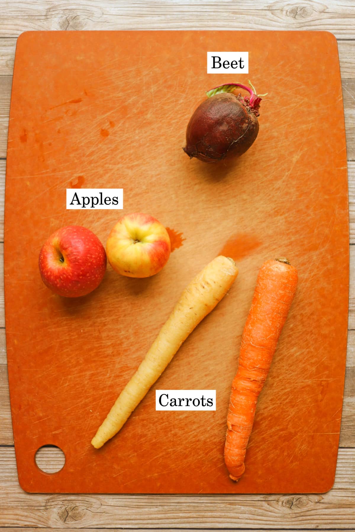 Labeled ingredients for apple, beet, carrot juice on cutting board.