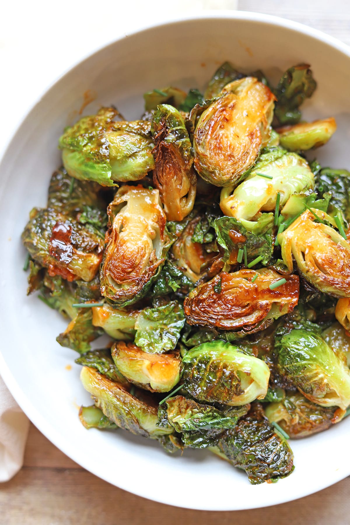 Fried Brussels sprouts tossed with gochujang glaze in white serving bowl.