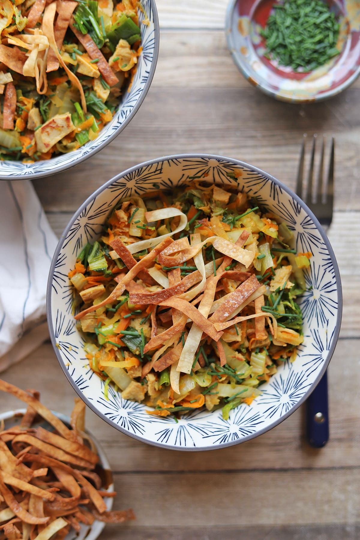 Crispy wontons on bowls with shredded cabbage, carrots, green onions, and vegan chicken.