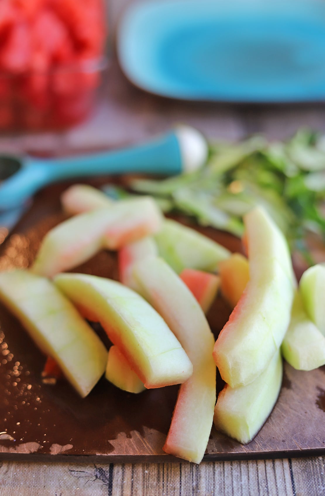 Slices of watermelon rind on cutting board with peeler and peels.