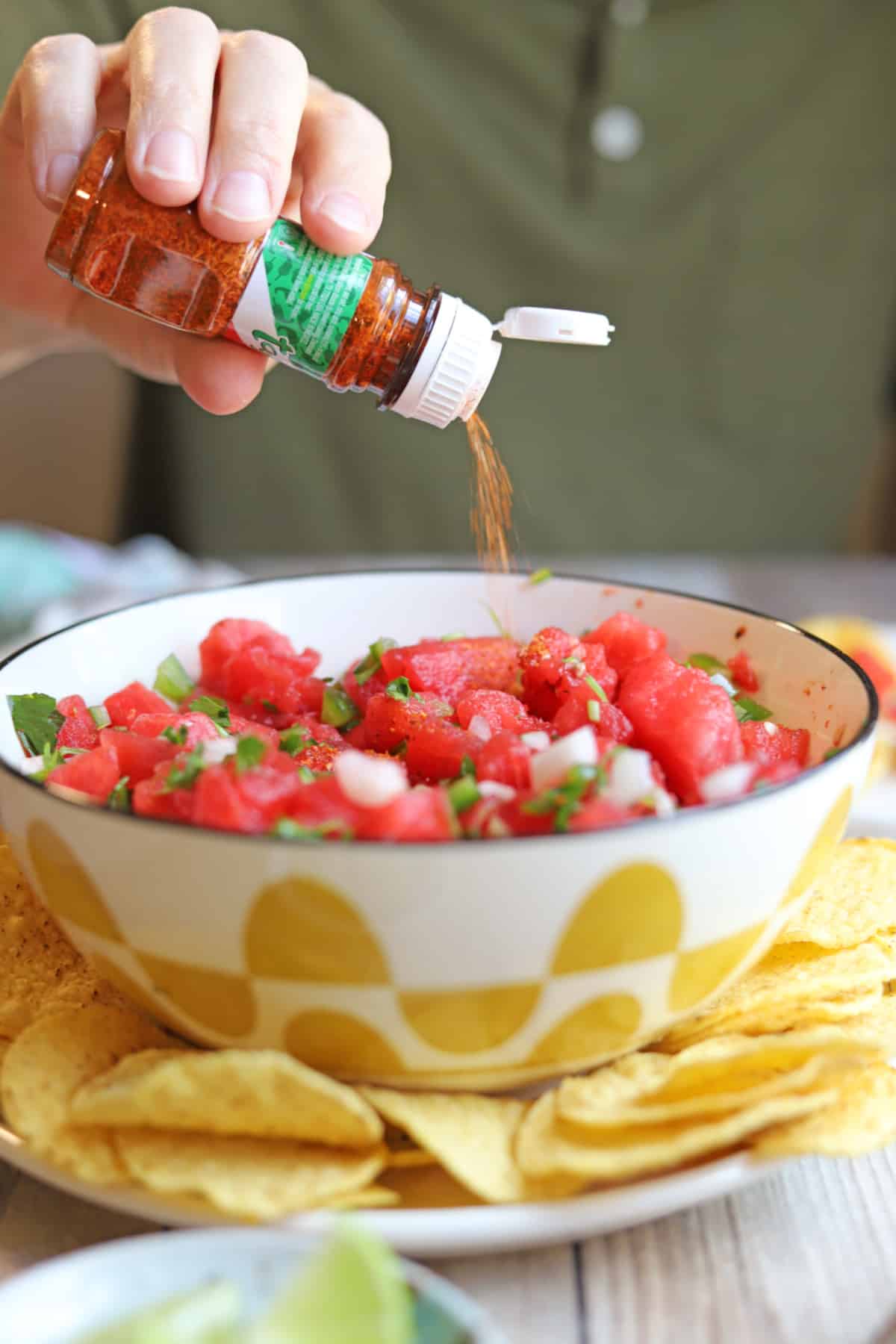 Tajin being sprinkled onto colorful bowl of watermelon salsa.