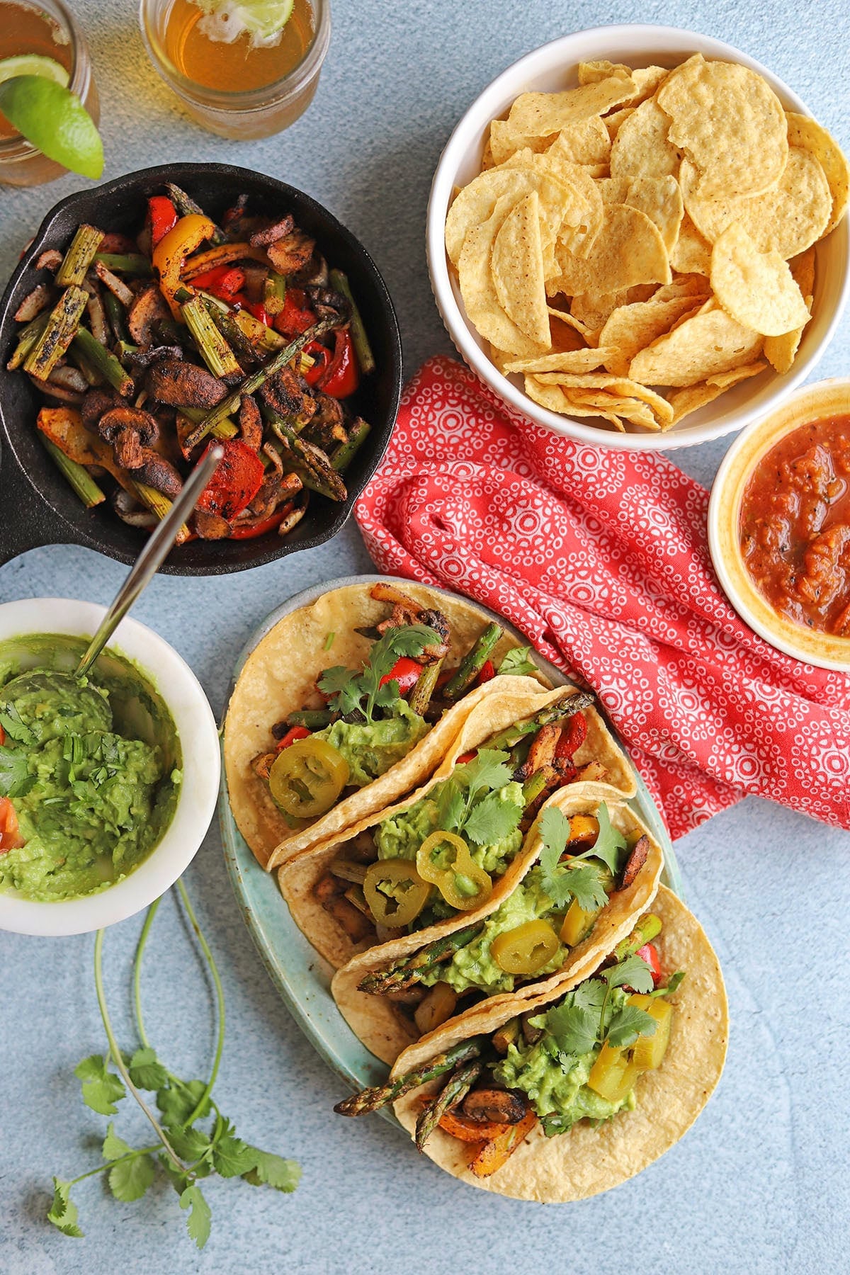 Table with grilled fajita vegetables, platter of fajitas, corn chips, salsa, and guacamole.