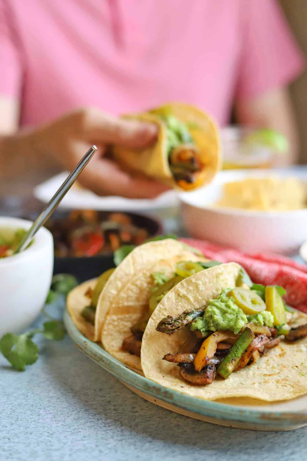 Hand holding fajitas in background behind platter of vegetable fajitas.