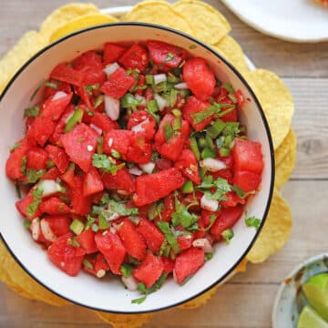 Watermelon salsa in bowl with diced fresh jalapeno, onion, and cilantro surrounded by tortilla chips.