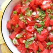 Text overlay: cadryskitchen.com, watermelon salsa. Bowl of bright red watermelon salsa dotted with cilantro in bowl.
