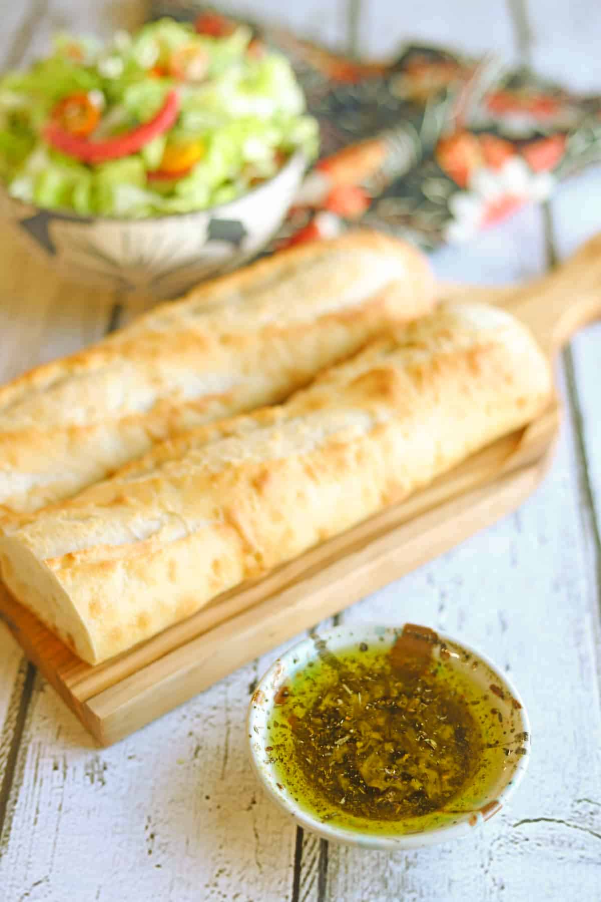 Restaurant-style Italian bread dip olive oil in serving bowl by baguette and salad.